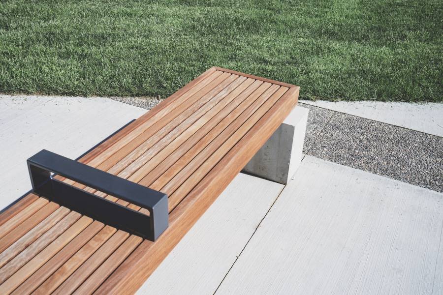 A timber bench on pale concrete beside a neatly kept lawn — clean, simple lines